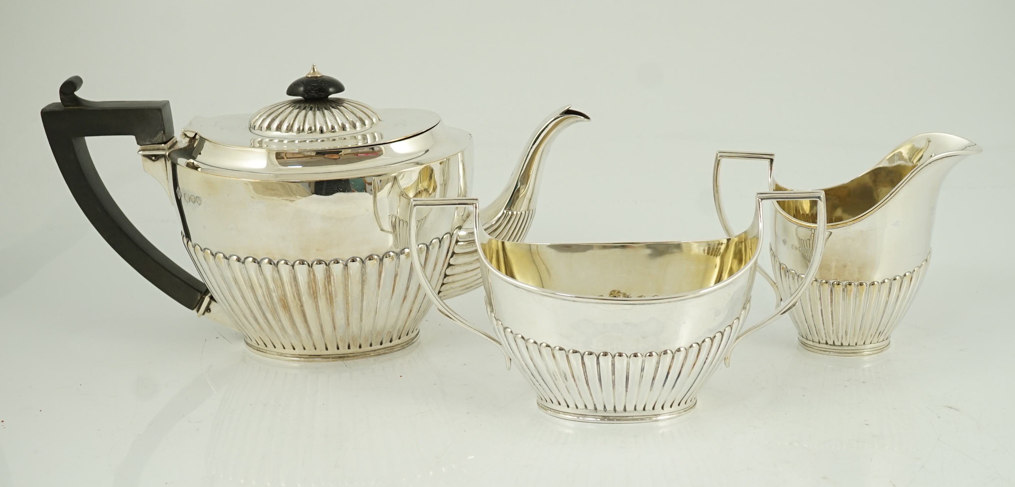 A late Victorian oak cased demi-fluted oval silver three piece tea set, by Martin, Hall & Co